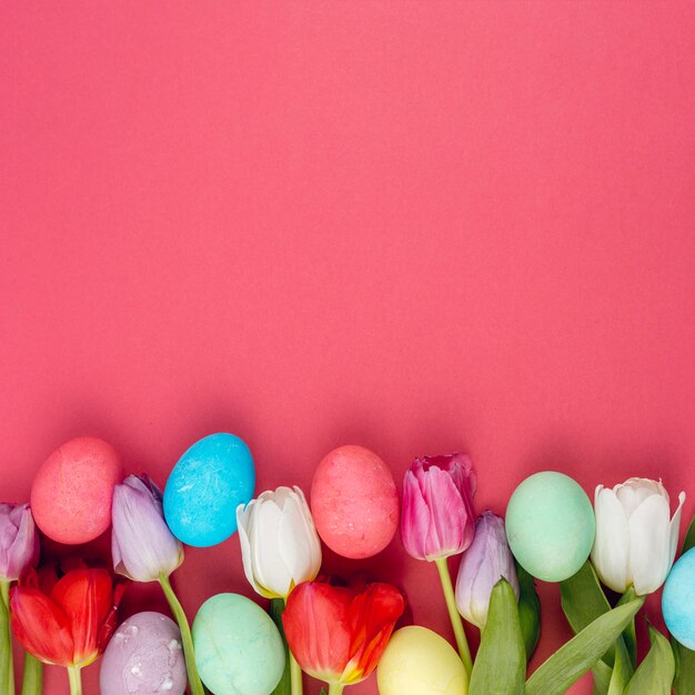 Coloridos huevos de Pascua con flores de tulipán en mesa roja
