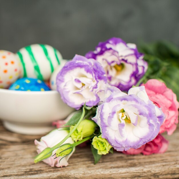 Coloridos huevos de pascua y lisianthus en mesa de madera