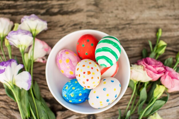 Coloridos huevos de pascua y lisianthus en mesa de madera