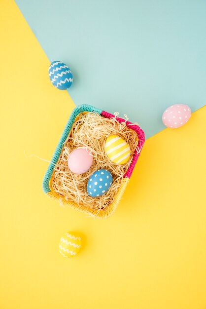 Coloridos huevos de Pascua en una pequeña canasta en mesa