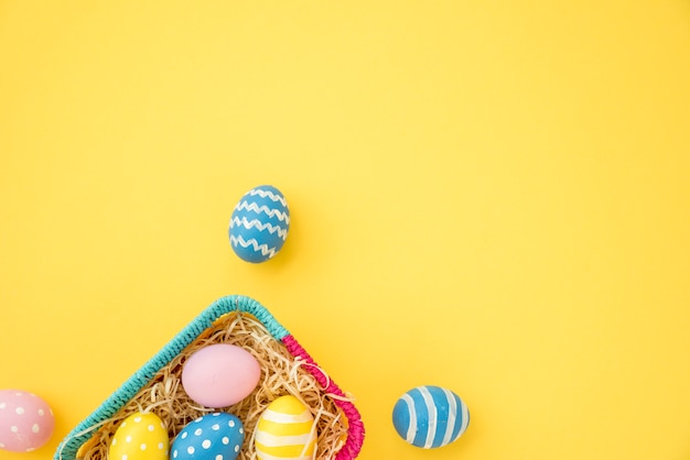 Coloridos huevos de Pascua en una pequeña cesta en mesa amarilla