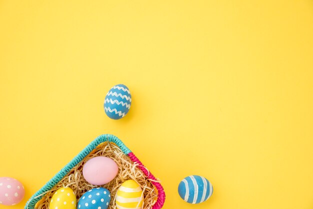 Coloridos huevos de Pascua en una pequeña cesta en mesa amarilla