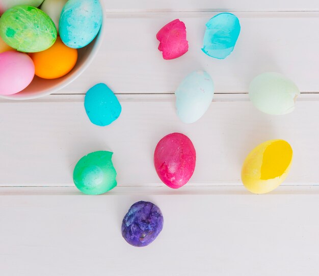 Coloridos huevos de Pascua en un tazón cerca de la cáscara en el escritorio