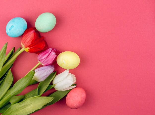 Coloridos huevos de Pascua con tulipanes en mesa roja