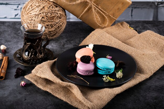 Coloridos macarons en un plato negro y un vaso de té sobre una mesa negra