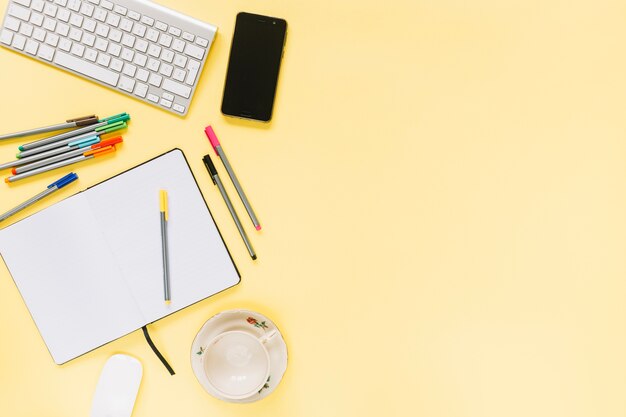 Coloridos rotuladores; portátil con teclado y teléfono móvil sobre fondo amarillo