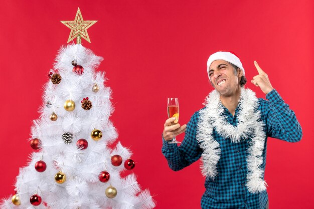 Cómico emocional feliz gracioso joven con sombrero de santa claus en una camisa de rayas azul sosteniendo una copa de vino