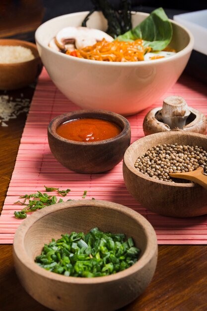 Comida asiática con tazón de madera de cebolla tierna y semillas de cilantro con salsa.