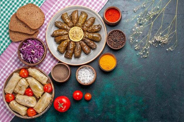 Comida de carne oriental de dolma de hojas de vista superior enrollada dentro de hojas verdes con condimentos y dolma de repollo en el plato de cena de carne de escritorio azul oscuro comida oriental