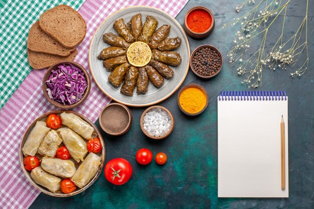 Comida de carne oriental de dolma de hojas de vista superior enrollada dentro de hojas verdes con condimentos y dolma de repollo en el plato de cena de carne de escritorio azul oscuro comida oriental