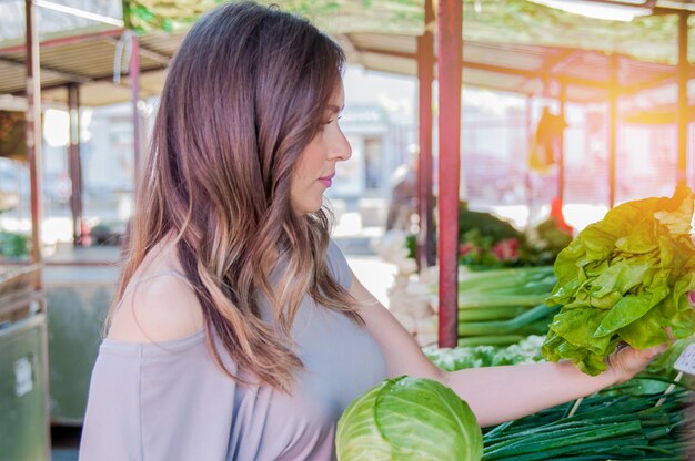 Comida cruda, concepto de vegetariano. Retrato de la muchacha sonriente bonita que mira en la ropa ocasional que sostiene la col en sus manos. Piel sana, cabello castaño brillante.