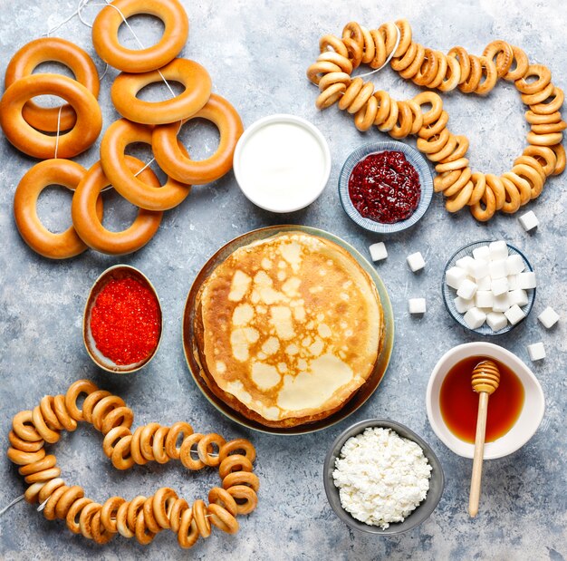 Comida del festival Shrovetide Maslenitsa. Panqueque ruso blini con mermelada de frambuesa, miel, crema fresca y caviar rojo, terrones de azúcar, requesón, bubliks a la luz