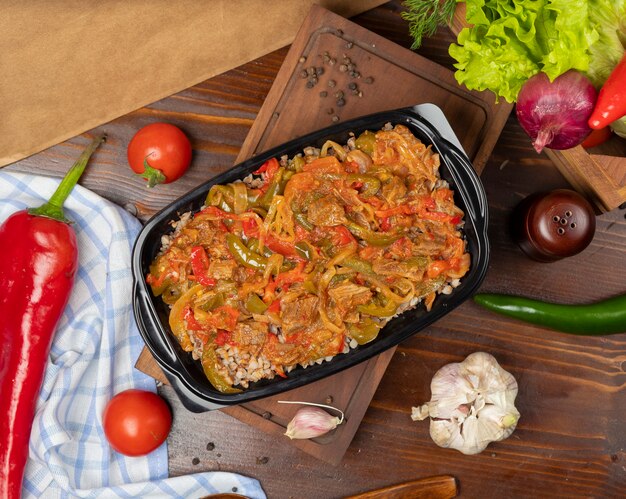 Comida para llevar de alforfón en un recipiente de plástico negro, comida dietética con salsa de cebolla y pimiento de tomate y pimiento