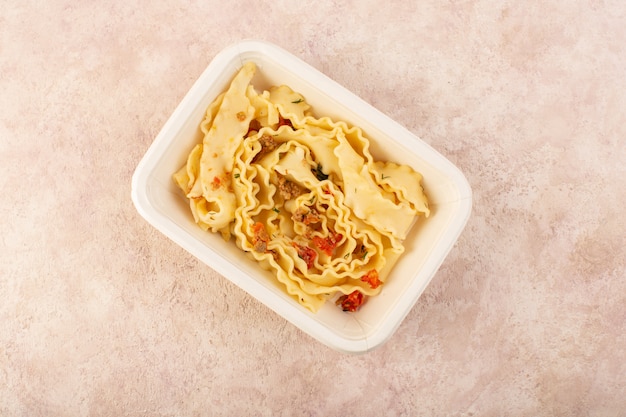 Una comida de masa de vista superior con tomates y carne dentro de un tazón blanco sobre rosa