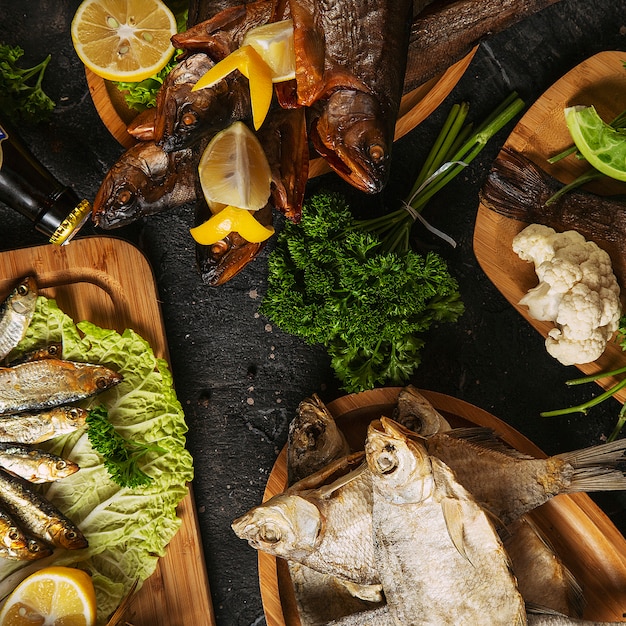 Comida mediterránea, pescado de arenque ahumado servido con cebolla verde, limón, tomates cherry, especias, pan y salsa Tahini en la oscuridad. Vista superior con un primer plano