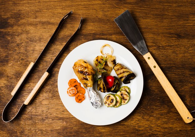 Comida a la parrilla en el plato y herramientas para asar