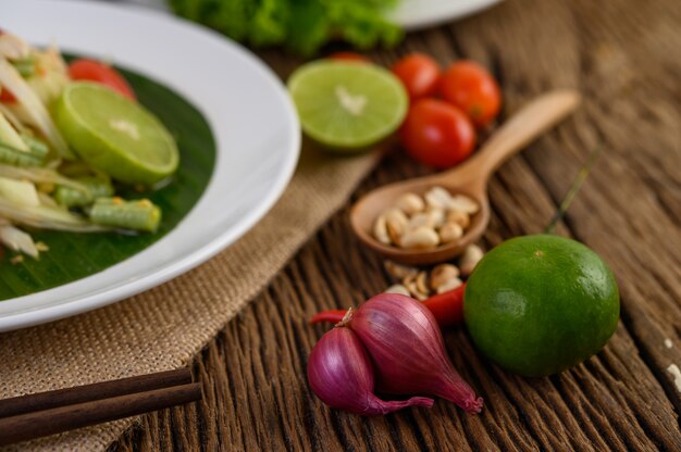 Comida picante de estilo tailandés, concepto de comida Som Tum, decoración de accesorios Ajo, limón, maní, tomate y chalotes en la mesa de madera