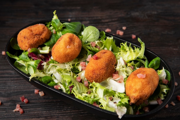 Comida que contiene croquetas con tocino y ensalada