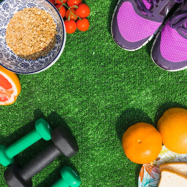 Comida saludable con par de zapatos deportivos y mancuernas sobre césped