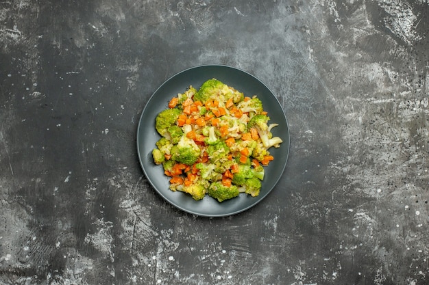 Comida sana con brocoli y zanahorias en una placa negra sobre mesa gris