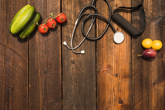 Comida sana con estetoscopio y correa de fitness en el fondo de madera