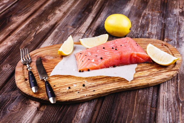 Comida sana y fresca. Salmón crudo servido con limones y cuchillos en tabla de madera