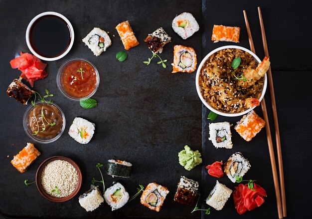Comida tradicional japonesa: sushi, rollos, arroz con camarones y salsa sobre un fondo oscuro. Vista superior