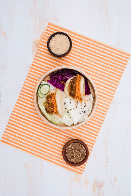 Comida tradicional de Taiwán gua bao emparedado al vapor en vaporera con cuencos de arroz y semillas de cilantro sobre el mantel