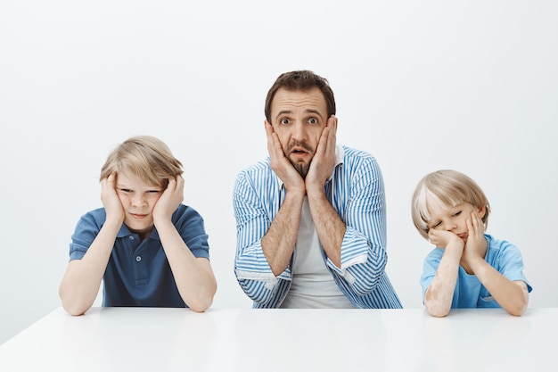 Cómo crecieron rápidamente. Retrato de un padre europeo ansioso conmocionado sentado con sus hijos, tomados de la mano en la cara y dejando caer la mandíbula