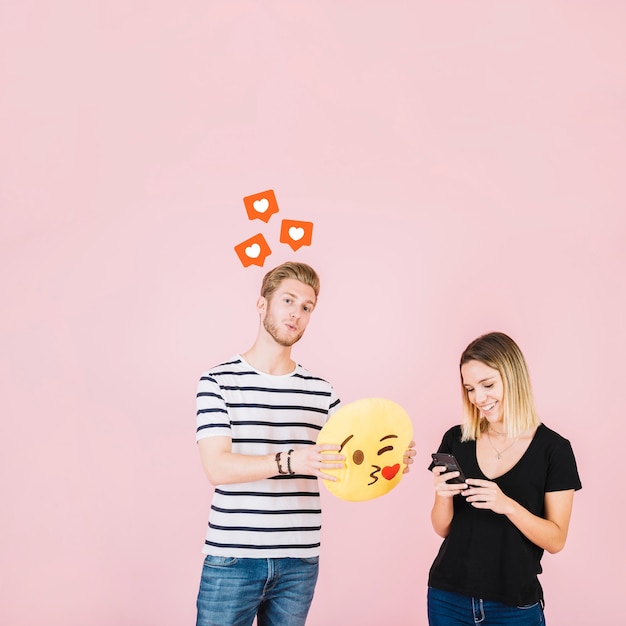 Como iconos sobre hombre sosteniendo beso emoji cerca de mujer feliz usando teléfono celular