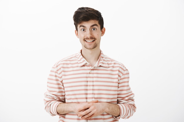 Foto gratuita como puedo ayudarte. retrato de asistente de tienda europeo atractivo y amable con camisa a rayas, tomados de la mano juntos y ofreciendo ayuda, hablando casualmente y cortésmente con el cliente sobre una pared gris