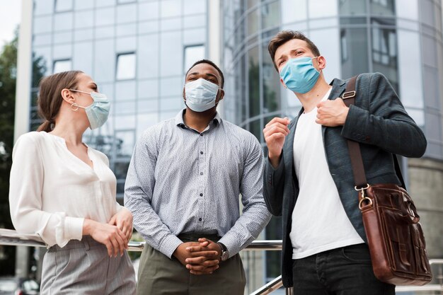 Compañeros charlando al aire libre durante la pandemia mientras usan máscaras médicas