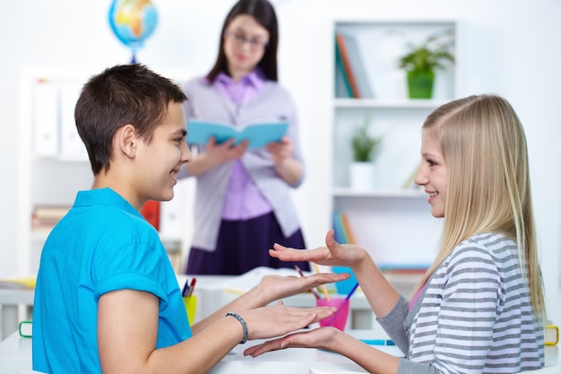 Compañeros de clase juguetones con la maestra de fondo