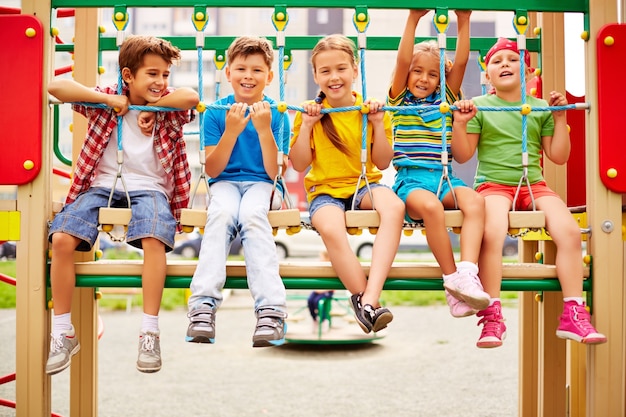 Compañeros de clase sonrientes sentados en fila en el parque infantil