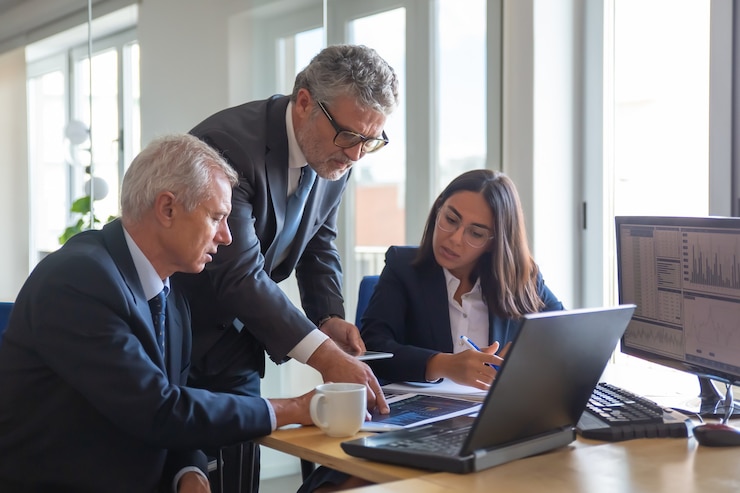 Foto gratuito compañeros concentrados mirando gráficos estadísticos y hablando sobre el trabajo. altos directivos profesionales y joven asistente preparando plan de negocios. concepto de trabajo en equipo, gestión y asociación