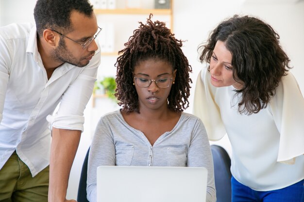 Compañeros confiados que hablan mientras trabajan con la computadora portátil