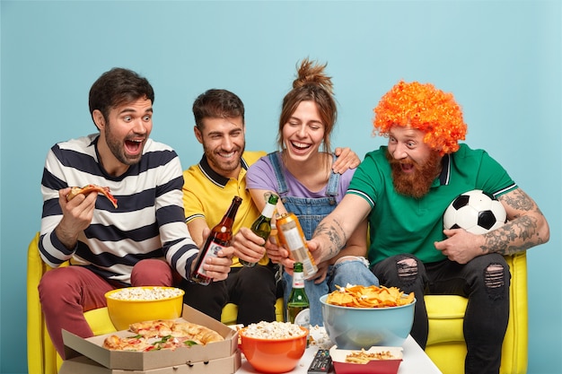 Compañeros de cuarto encantados en el apartamento celebran la victoria de su equipo favorito, tintinean botellas con cerveza