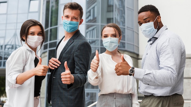 Compañeros de trabajo al aire libre durante la pandemia con máscaras y dando pulgar hacia arriba