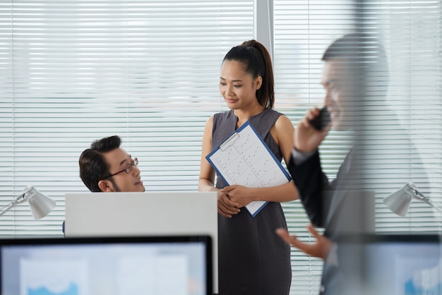 Compañeros de trabajo asiáticos discutiendo algo mientras su colega hablando por teléfono