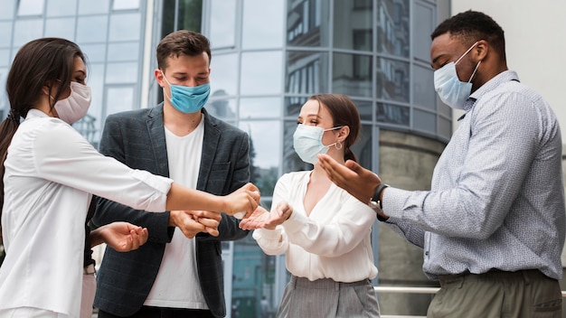 Compañeros de trabajo desinfectando sus manos al aire libre durante una pandemia mientras usan máscaras