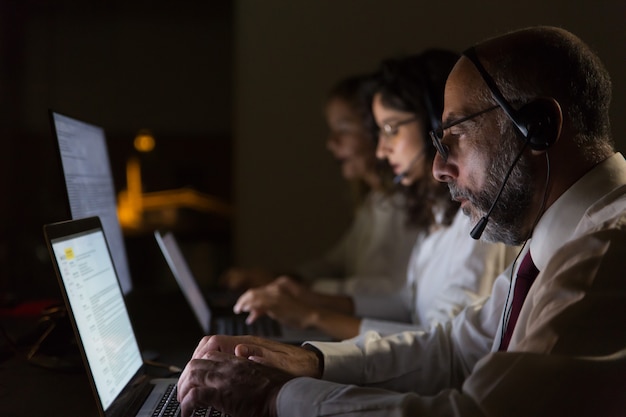 Compañeros de trabajo enfocados en auriculares escribiendo en computadoras portátiles