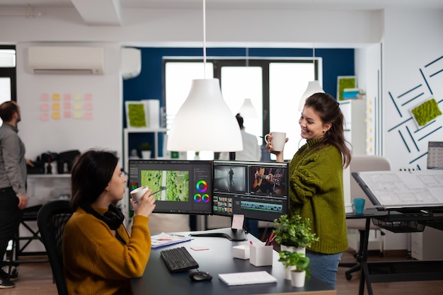 Compañeros de trabajo felices hablando de montaje de película mirando imágenes de película trabajando en la oficina de la agencia de inicio creativo con dos monitores