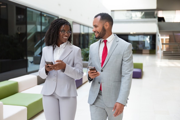 Compañeros de trabajo felices usando teléfonos móviles y chateando