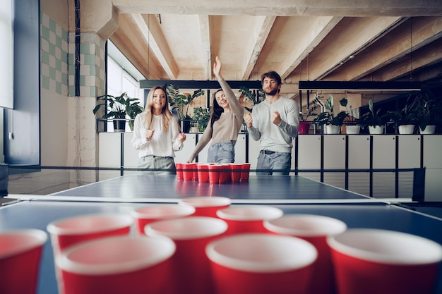 Foto gratuita compañeros de trabajo jóvenes jugando beer pong en la oficina moderna