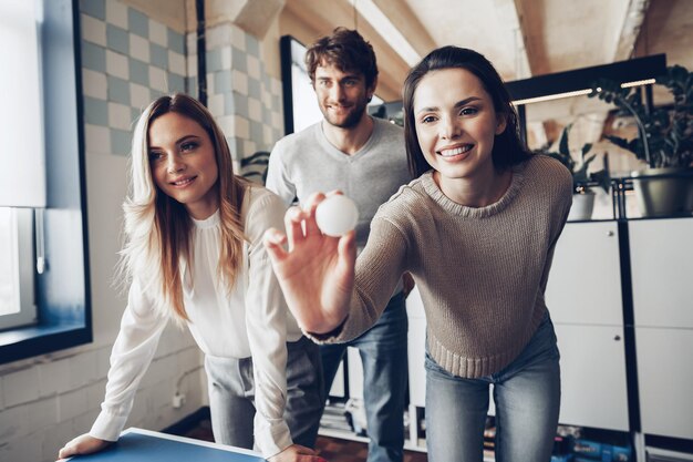 Compañeros de trabajo jóvenes jugando beer pong en la oficina moderna