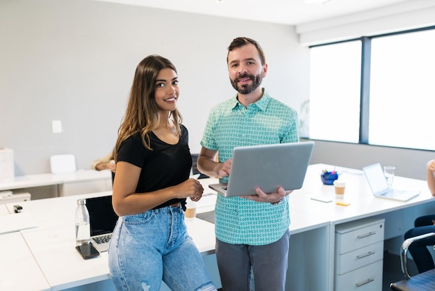 Compañeros de trabajo masculinos y femeninos confiados que planean sobre la computadora portátil en el escritorio en la oficina