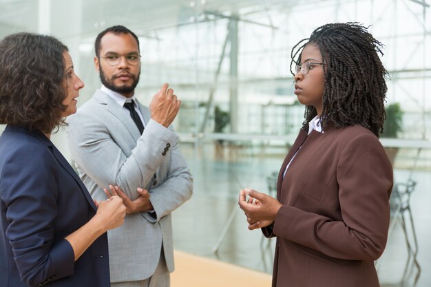 Compañeros de trabajo multiétnicos serios discutiendo proyecto afuera