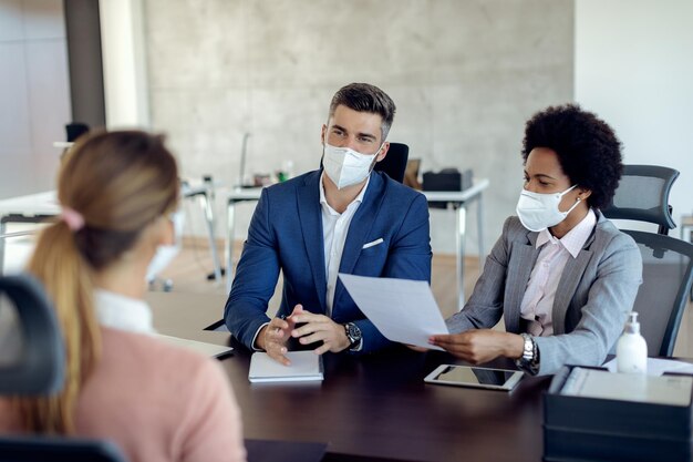 Compañeros de trabajo de negocios que usan máscaras faciales mientras hablan con un posible candidato en la oficina
