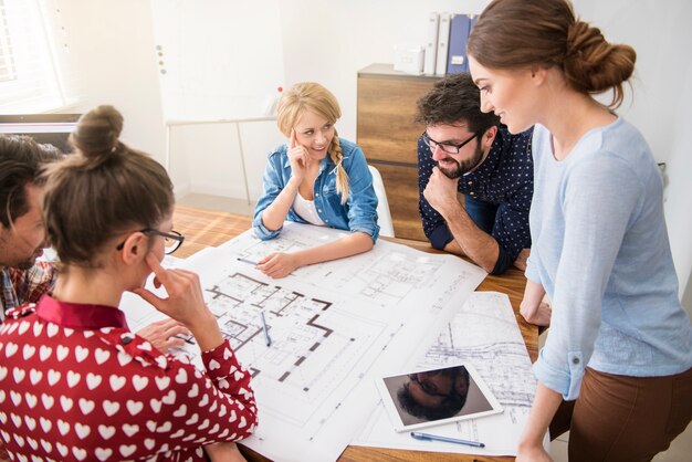 Foto gratuita compañeros de trabajo en la oficina con planos de arquitectura y una computadora