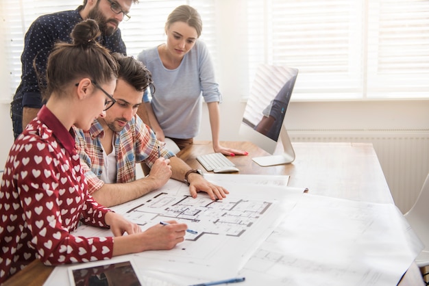 Compañeros de trabajo en la oficina con planos de arquitectura y una computadora